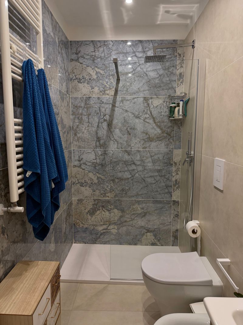 Bagno con doccia rivestita in marmo grigio-azzurro e asciugamani blu
