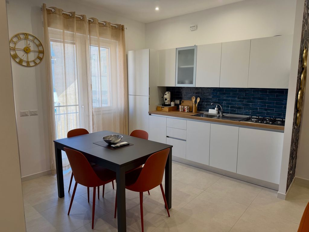 Cucina bianca con piastrelle blu e tavolo da pranzo accanto alla finestra