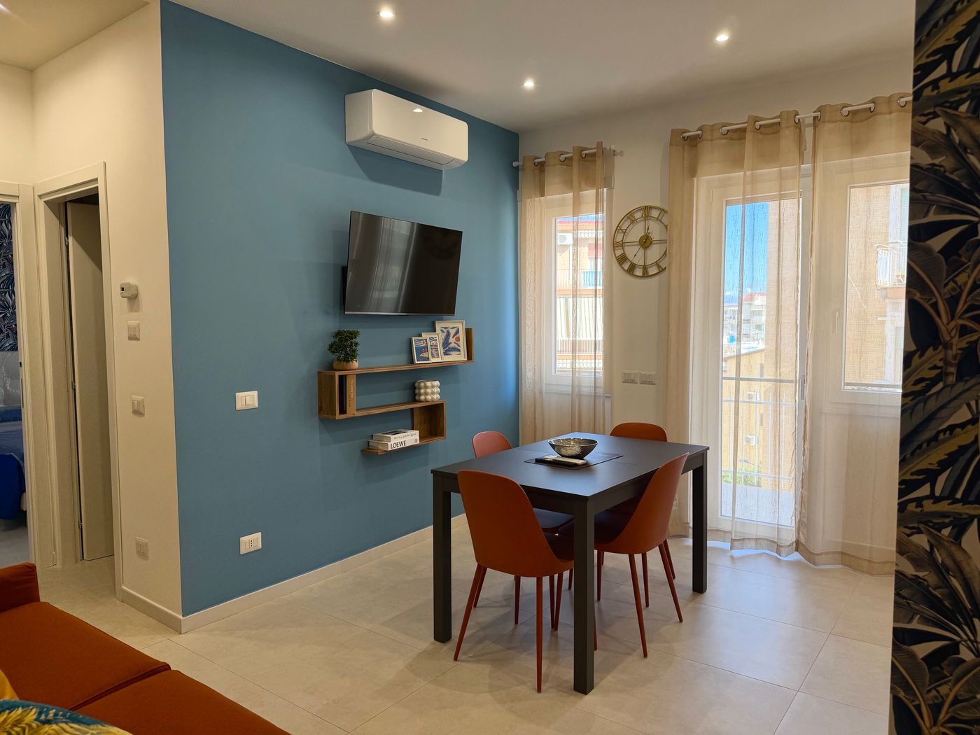 Zona pranzo con parete azzurra, Smart TV e luce naturale dalla finestra