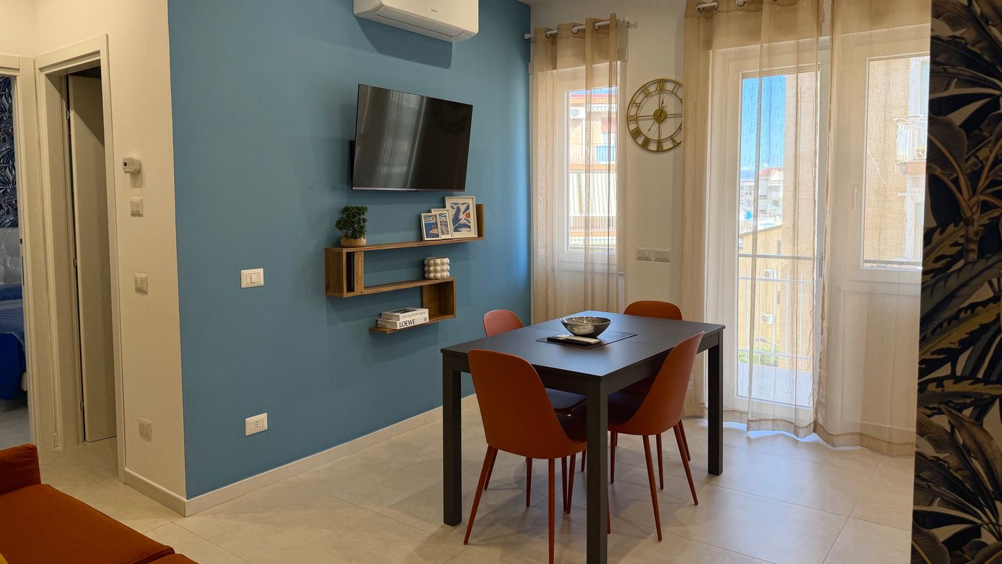 Zona pranzo con parete azzurra, Smart TV e luce naturale dalla finestra