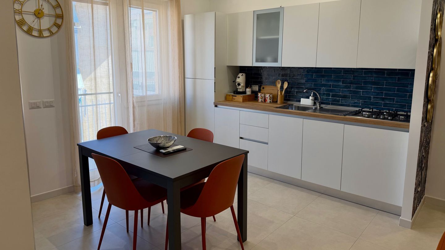 Cucina bianca con piastrelle blu e tavolo da pranzo accanto alla finestra