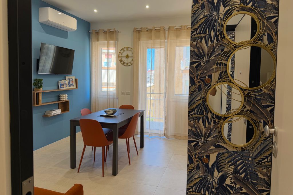 Soggiorno con parete azzurra, tavolo da pranzo e sedie color terracotta, visto dall'ingresso